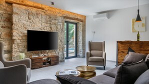A modern living room with stone walls, a flat-screen TV, a comfortable sofa, and a wooden sideboard. - Villa Vittorina (Pusti)