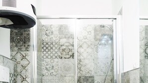 Un baño moderno con cabina de ducha de vidrio, azulejos estampados, un inodoro blanco y un lavabo con espejo.