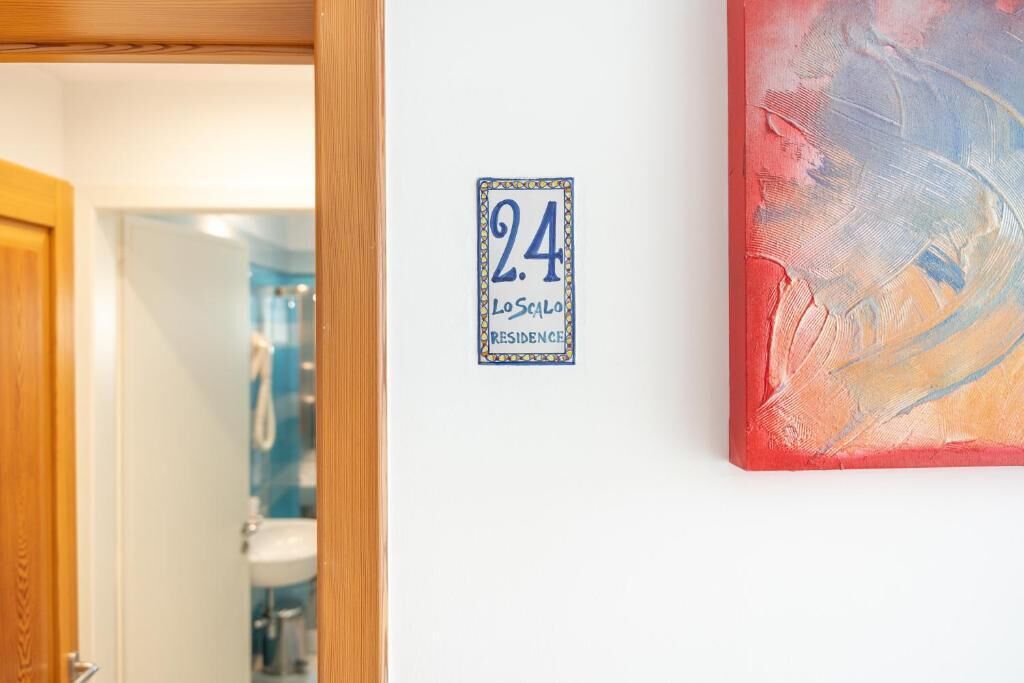 Une pièce avec une porte donnant sur une salle de bain, une plaque fixée au mur indiquant le numéro de chambre 24, et une vue partielle d’une peinture abstraite aux couleurs vives.