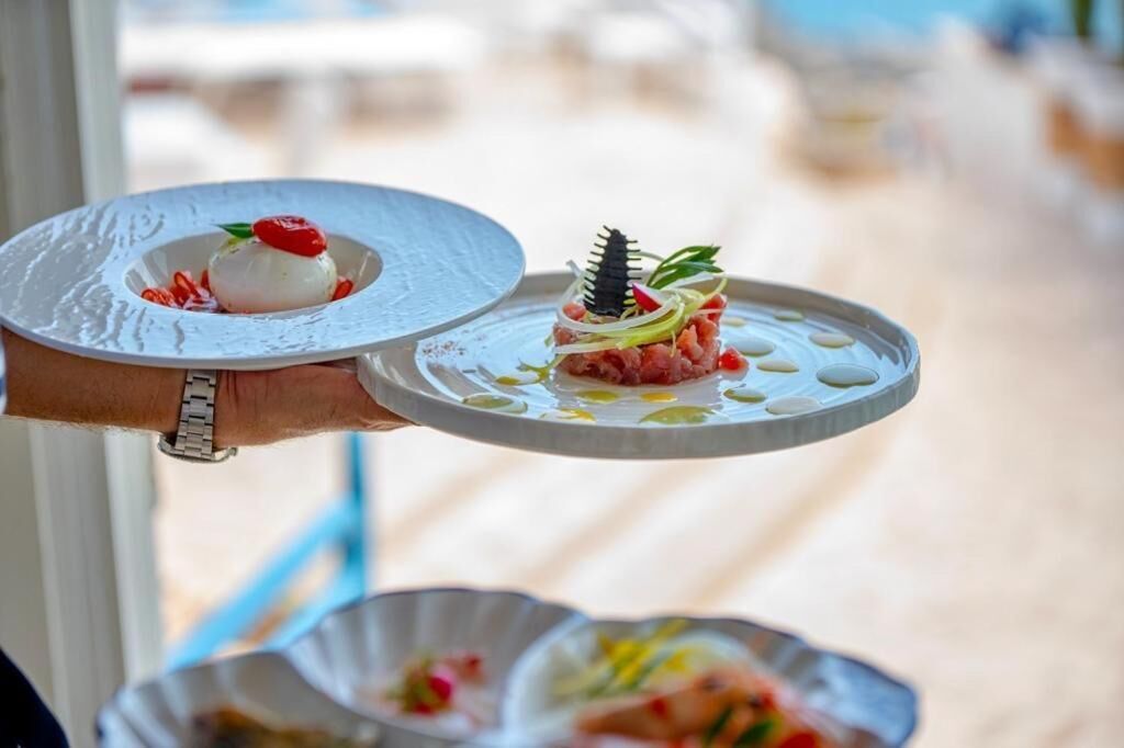 Une personne tenant deux assiettes de plats de fruits de mer, l’une garnie d’une cerise et l’autre d’un élément décoratif.