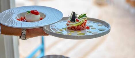 Une personne tenant deux assiettes de plats de fruits de mer, l’une garnie d’une cerise et l’autre d’un élément décoratif.