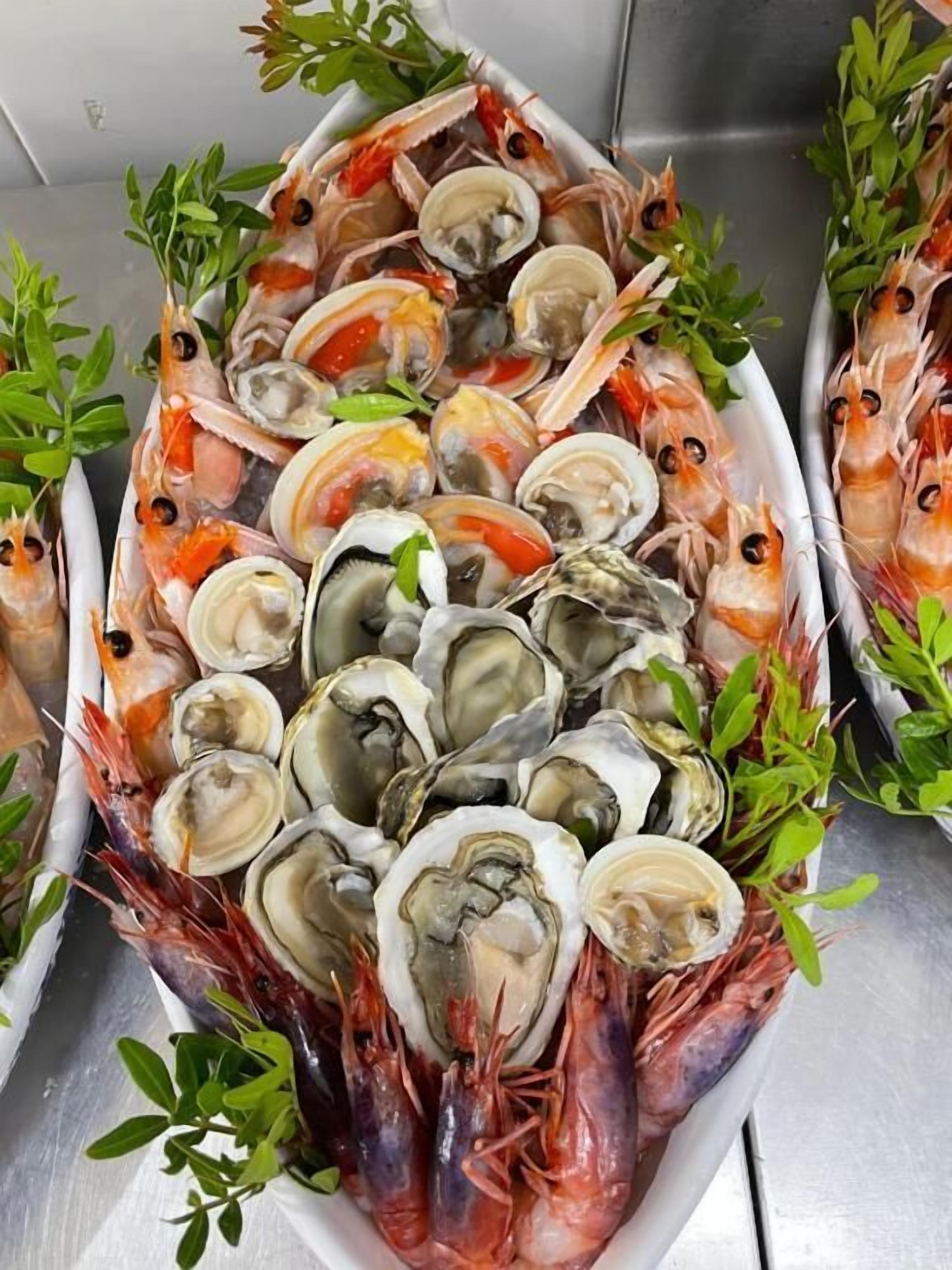 Eine Fischplatte mit Austern, Miesmuscheln und Garnelen, umgeben von grünen Blättern.