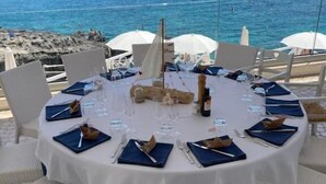 A round table set for dining with white tablecloths and blue napkins, overlooking a rocky coastline and the sea. - Lo Scalo bed and breakfast (Alessano)