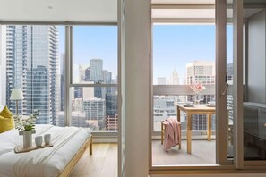 Ein modernes Schlafzimmer mit großem Fenster und Blick auf die Stadt, einem Bett mit Tablett und einem kleinen Tisch mit Stuhl.