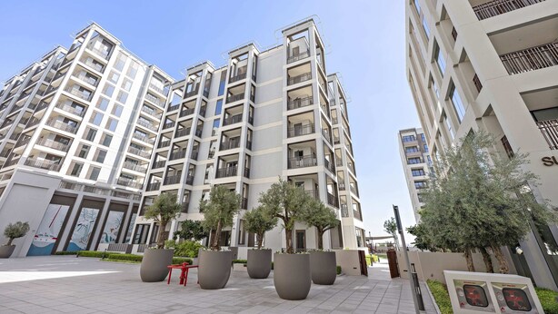 A modern multi-story residential building with balconies, large planters, and a clear sky. - Silkhaus Summer Towers Creek Harbour (Dubai)