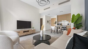 A modern living room with a flat-screen TV, a sofa, a coffee table, and a dining area with a kitchen in the background. - Silkhaus Summer Towers Creek Harbour (Dubai)