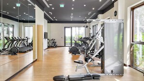 A gym with exercise equipment, large windows, and a mirror wall. - Silkhaus Summer Towers Creek Harbour (Dubai)