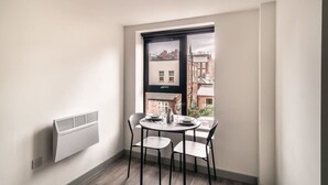 A corner room with a table and chairs, a window with a view of buildings, and a wall-mounted radiator. - Cozy 1-BR | Steps from Liverpool Centre (Liverpool)