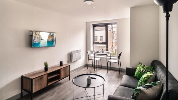 A modern living room with a flat-screen TV, a round coffee table, a sofa, and a dining area with chairs. - Cozy 1-BR | Steps from Liverpool Centre (Liverpool)