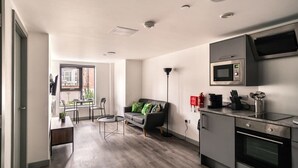 A modern kitchen with a built-in microwave and oven, a dining area with a table and chairs, and a cozy seating area with a sofa and floor lamp. - Cozy 1-BR | Steps from Liverpool Centre (Liverpool)