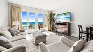 Un salón amplio con un sofá grande, un televisor de pantalla plana y vistas a la playa a través de amplios ventanales correderas.
