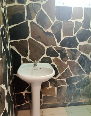 A bathroom with a white pedestal sink against a stone wall. - Baan Rai Somkiat Homestay (Pak Chong)