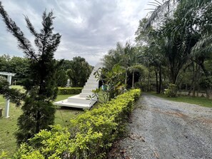 A pathway leading to a white staircase surrounded by lush greenery and trees. - Baan Rai Somkiat Homestay (Pak Chong)