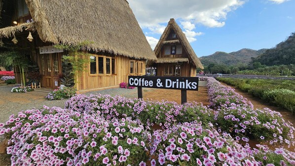 A rustic building with a thatched roof, a sign for coffee & drinks, and a flower garden. - Baan Rai Somkiat Homestay (Pak Chong)