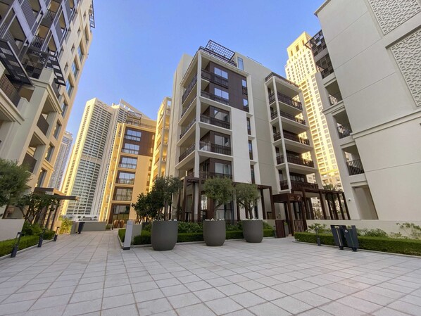 Un edificio residencial moderno con varios pisos, balcones y un amplio patio con plantas en macetas.