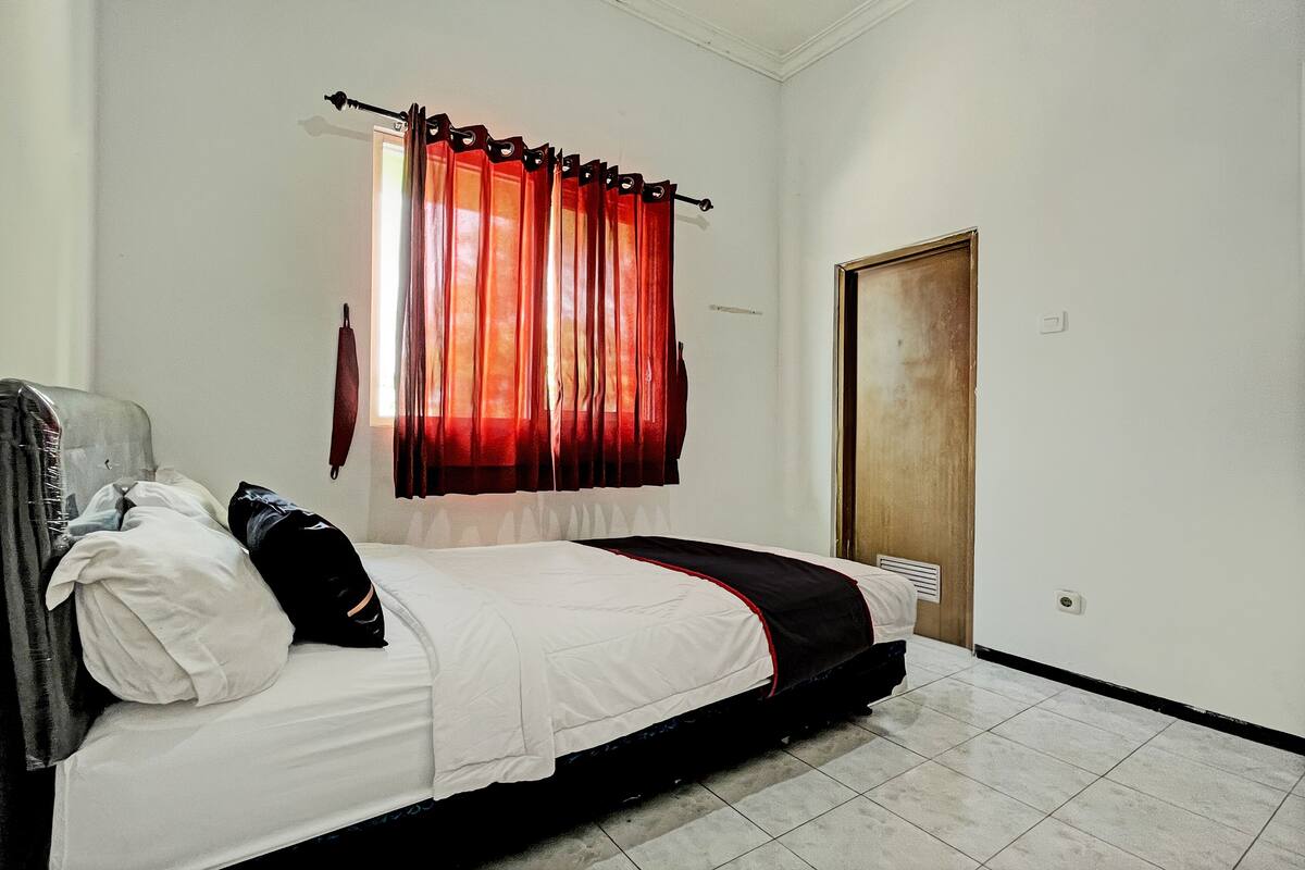A single bed with a white and black bedspread, a red curtain, and a wooden door.