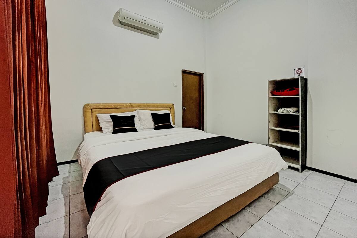 A neatly made bed with a wooden headboard, a white and black bedspread, and a red curtain on the left.