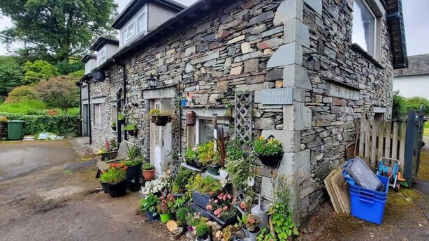 Ein Steinhaus mit einem Schild, auf dem „FAIRFIELD COTTAGE“ steht, und verschiedenen Kübelpflanzen und Blumen davor.