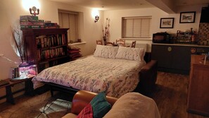 Un dormitorio acogedor con una cama grande, una estantería, un escritorio con computadora y una ventana con persianas.