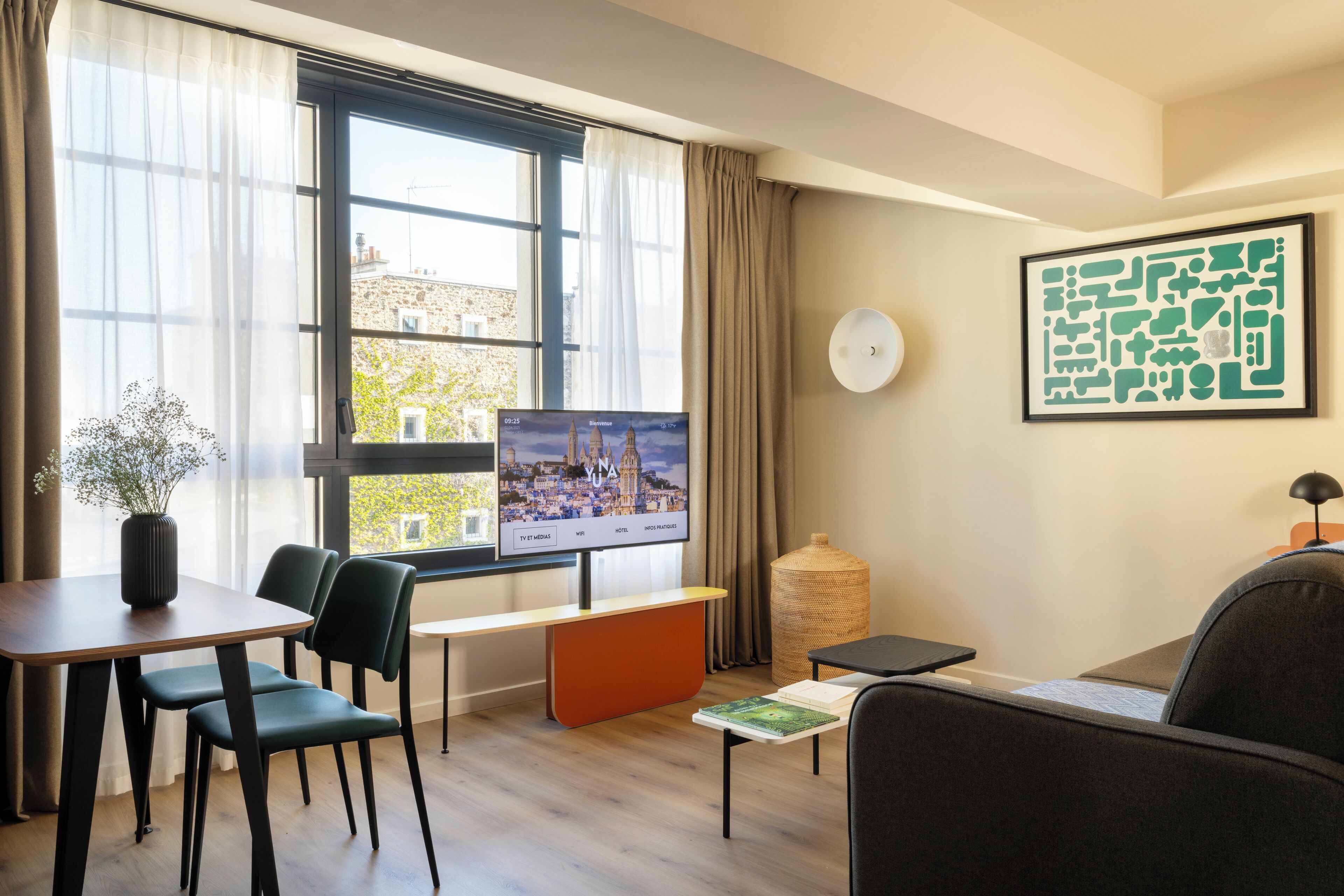Una habitación de hotel moderna con un ventanal grande, un televisor de pantalla plana, un área de comedor con mesa y sillas, un sofá, una mesita auxiliar pequeña y un jarrón decorativo.