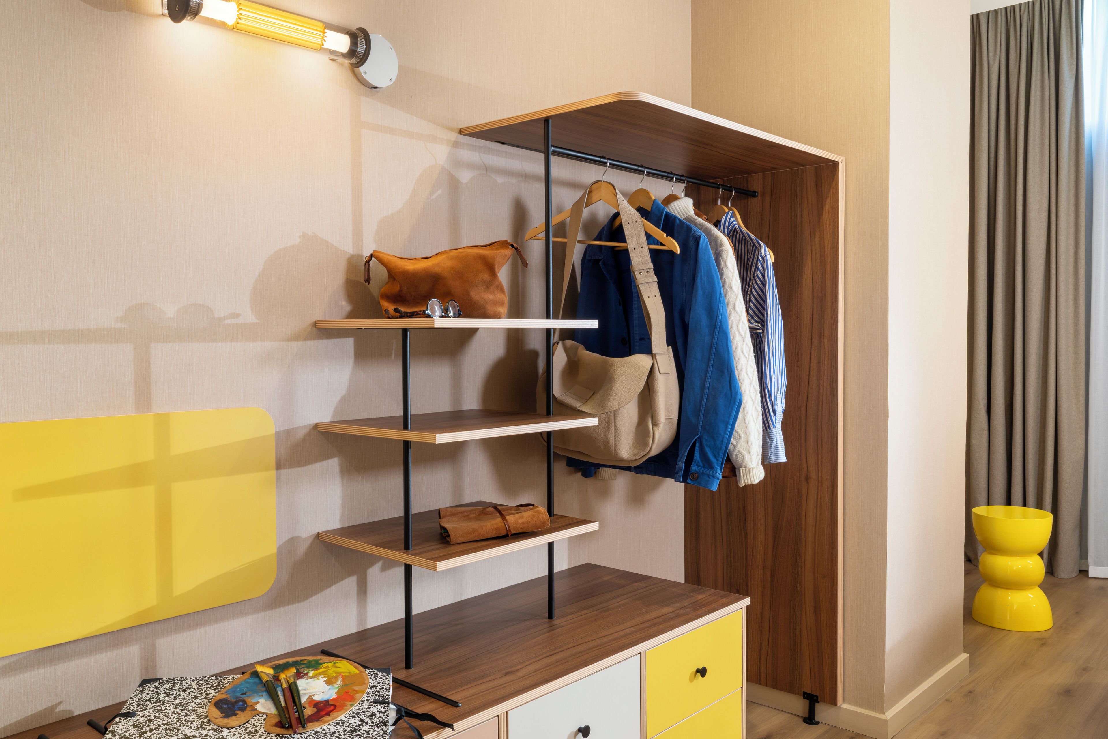 A modern room with a wooden desk, a yellow cabinet, and a clothing rack with hanging garments.
