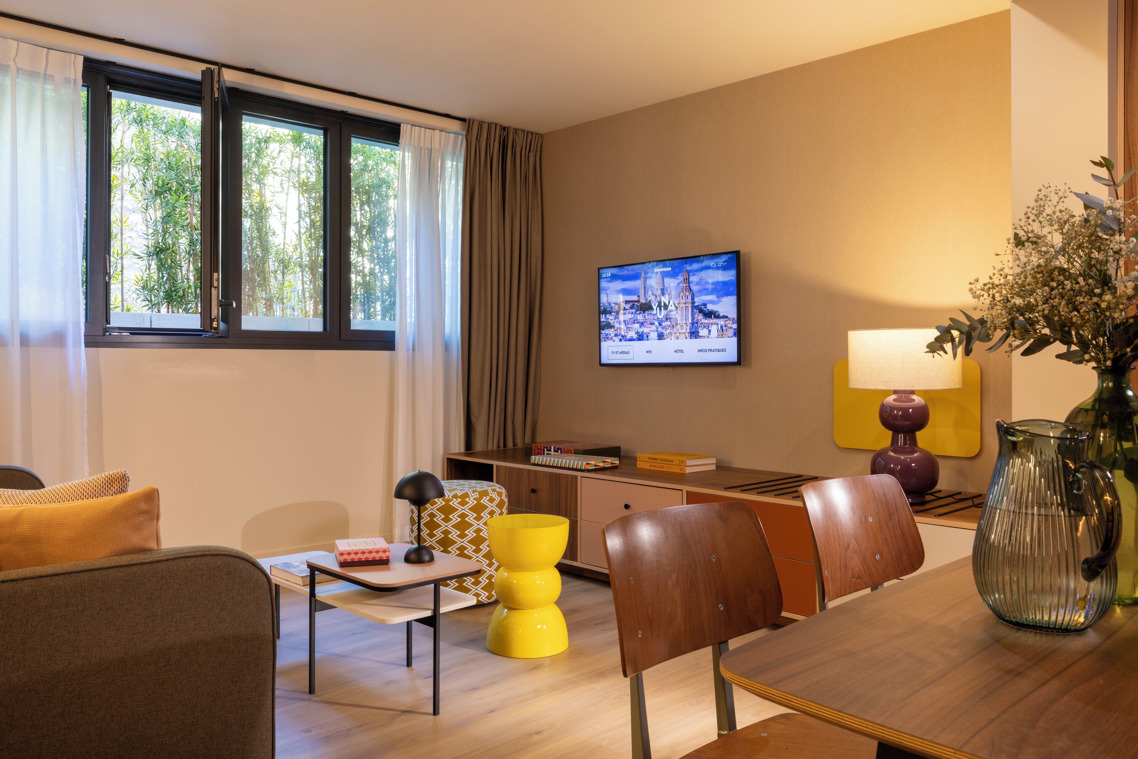 A modern living room with a sofa, a coffee table, a TV mounted on the wall, and a window with curtains.