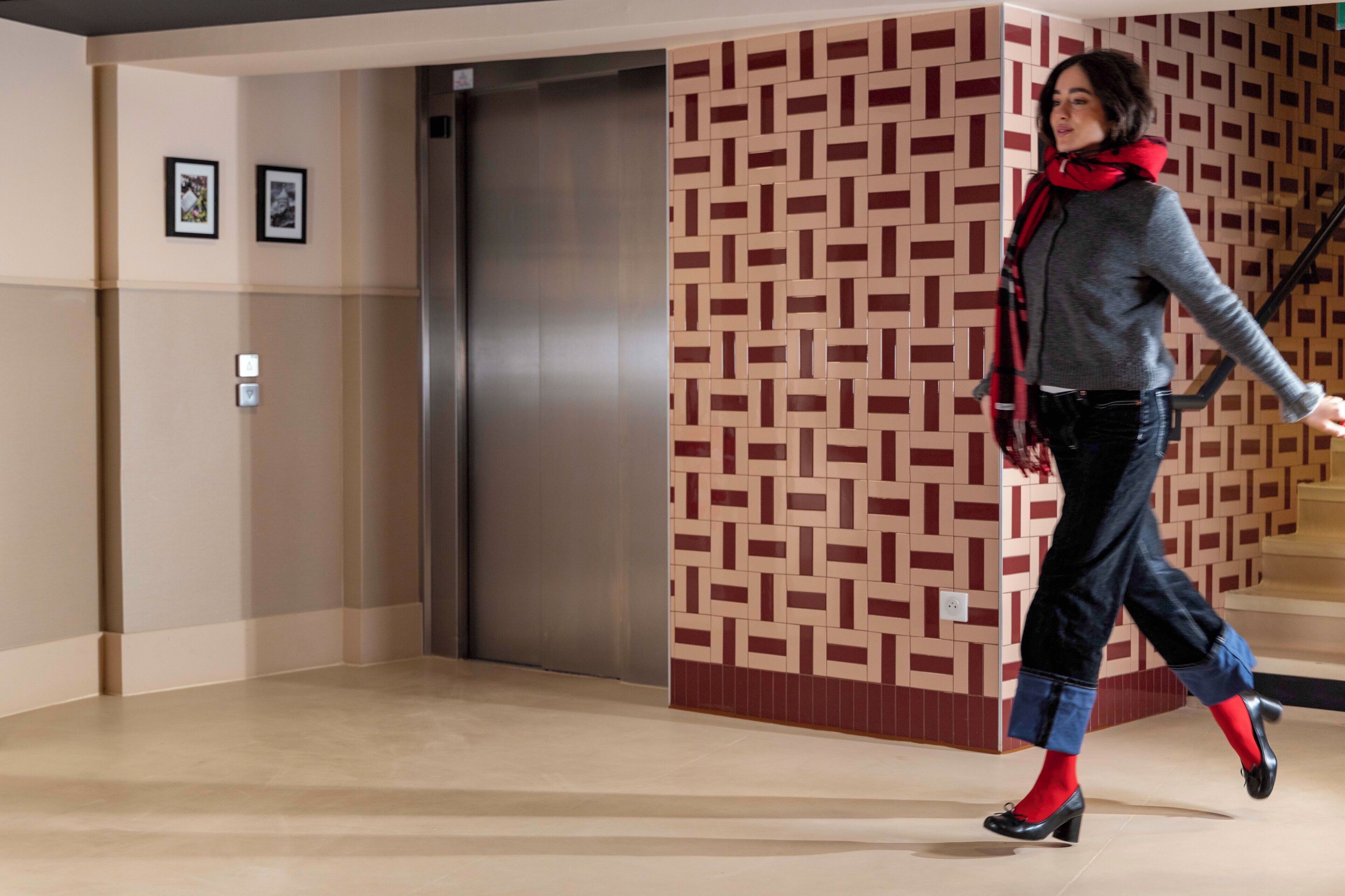 A modern elevator with a geometric patterned wall, a polished floor, and a staircase with a handrail.
