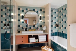 A modern bathroom with a glass-enclosed shower, a large round mirror with lights, a white sink, and a bathtub. - Yuna Montmartre - ApartHotel (Paris)