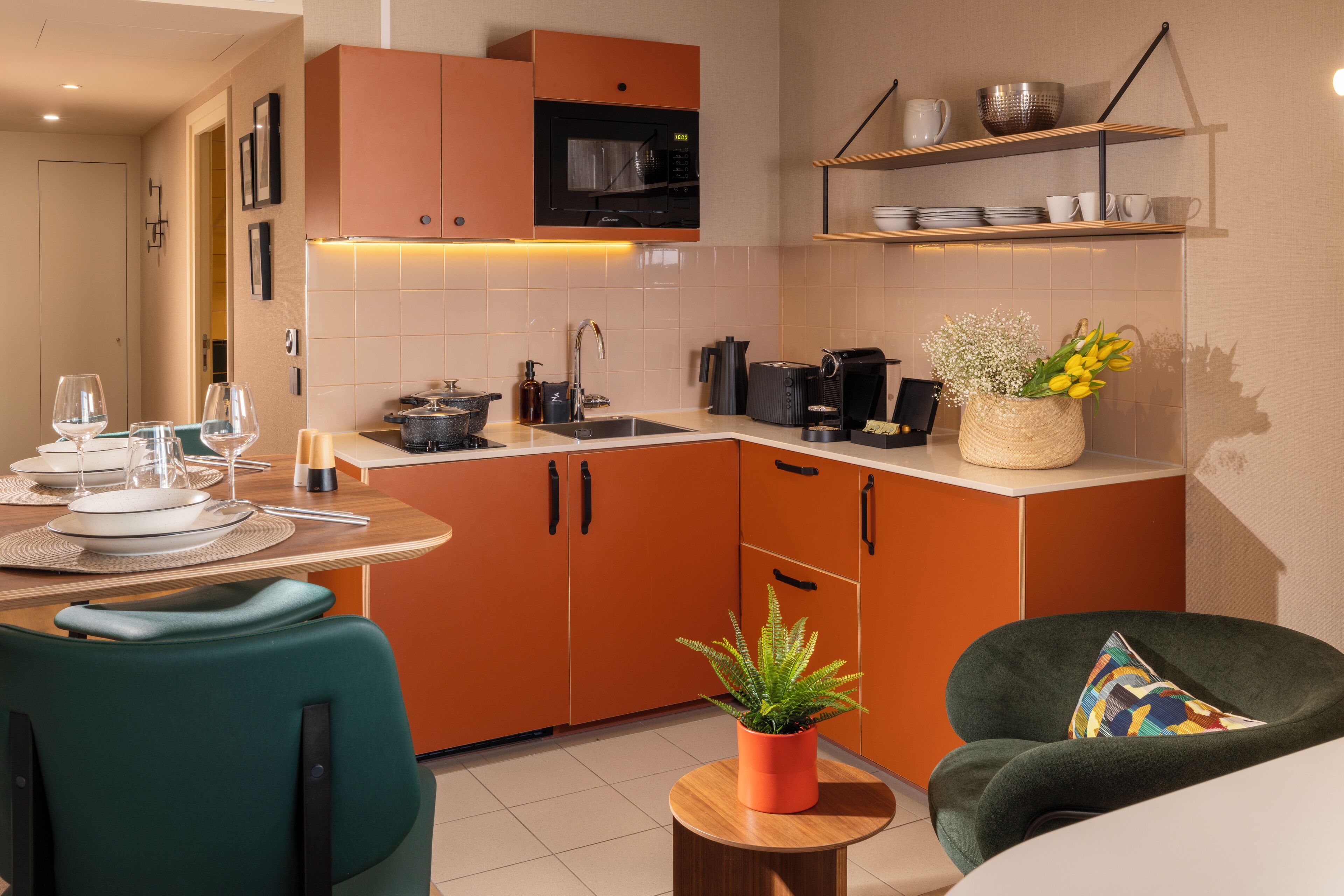 Una cocina moderna con armarios color naranja, un microondas y un lavamanos. Hay una mesa de comedor con sillas y una planta en maceta.