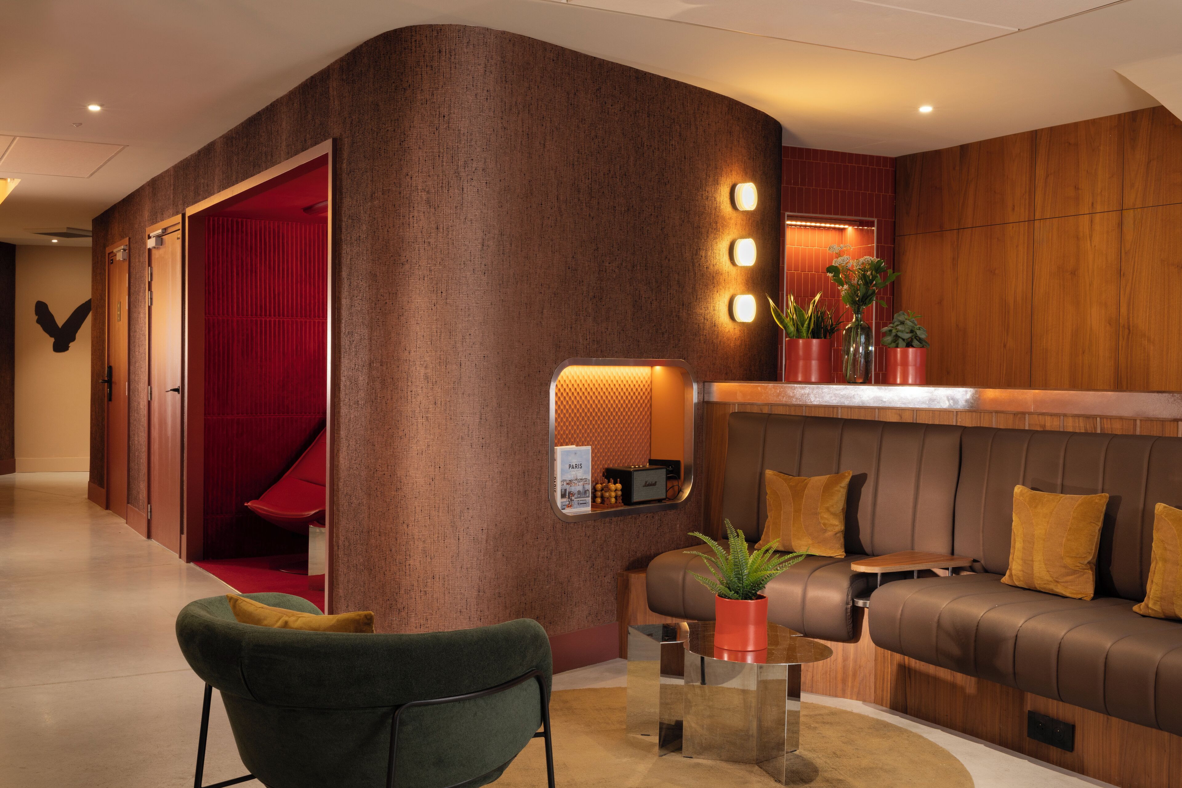 A modern lobby with a red accent wall, a reception desk, a sofa, and a green armchair.