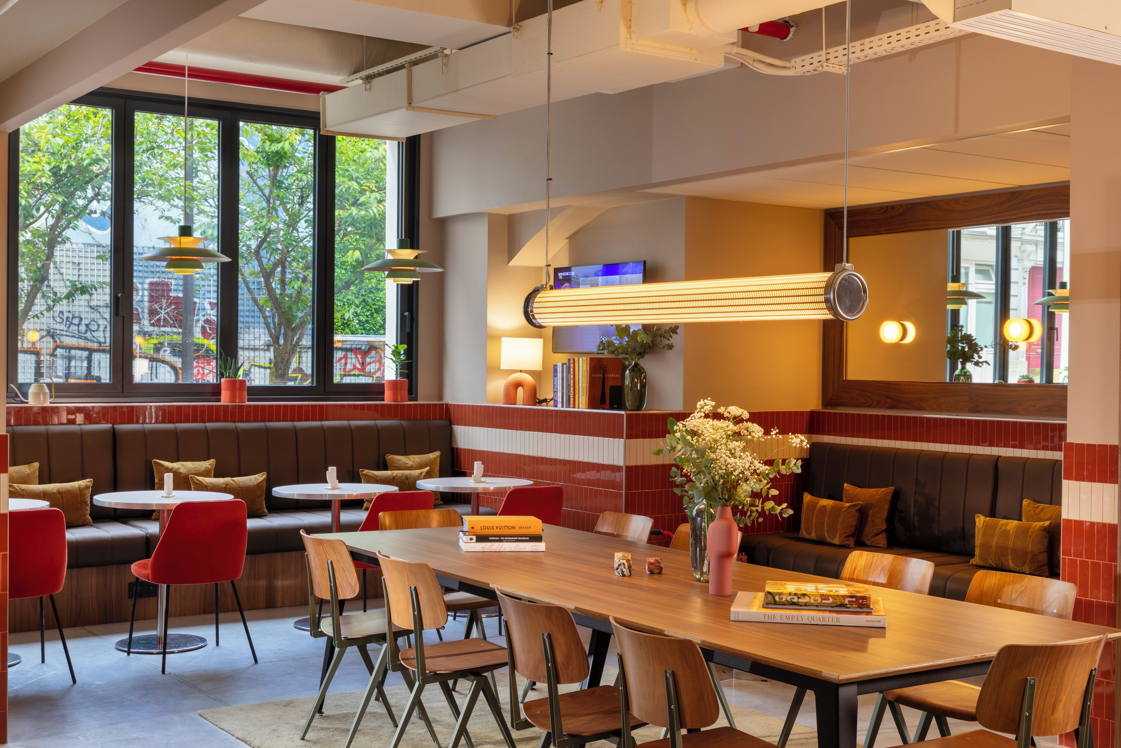 Un intérieur de restaurant moderne, avec différents types de sièges, notamment des banquettes et des tables, une grande fenêtre offrant une vue sur la ville et une variété de luminaires.