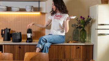 A woman sitting at a kitchen counter with a coffee maker, a basket, and a vase with flowers.