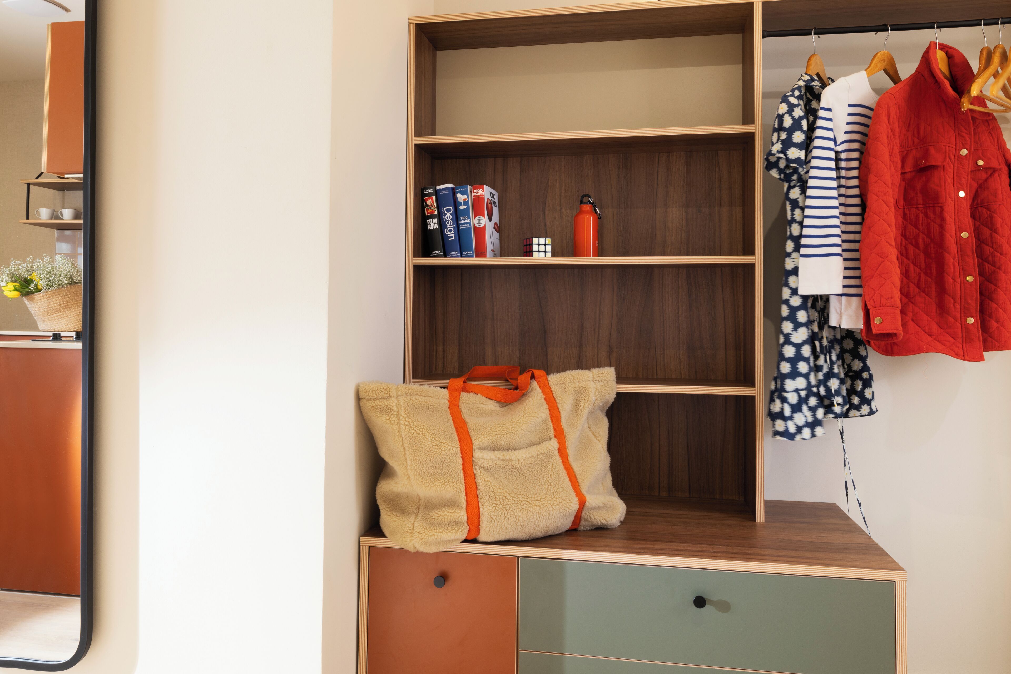 A wardrobe with multiple shelves, a hanging rack, and a small table with a bag and books.