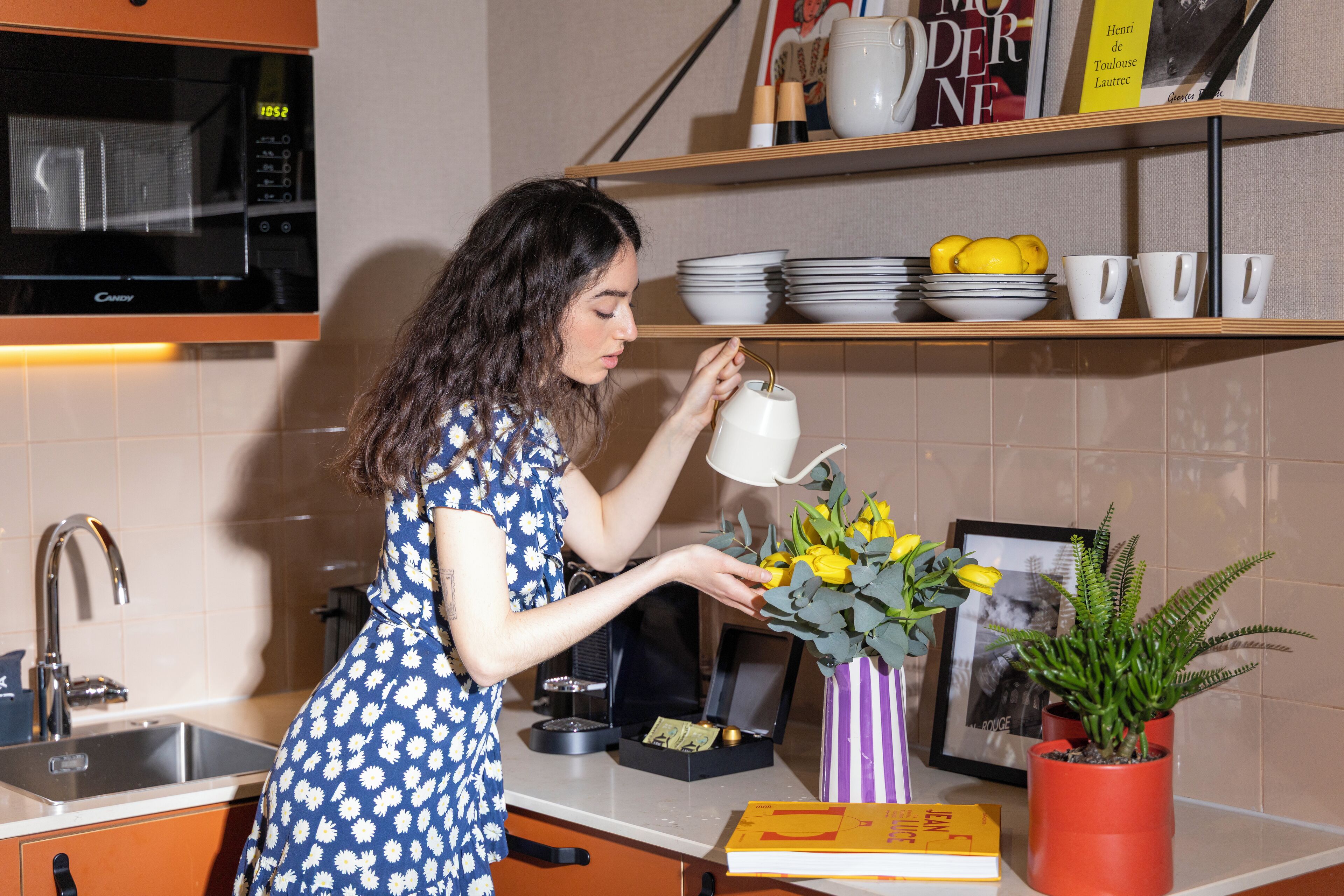 A kitchen with a microwave, sink, and shelves with dishes and a book.