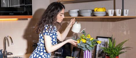 A kitchen with a microwave, sink, and shelves with dishes and a book.