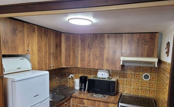 Une cuisine compacte avec des meubles en bois, un réfrigérateur blanc, un four à micro-ondes et une machine à café Bosch.