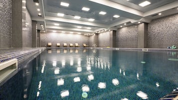 Una piscina con paredes de azulejos, luces en el techo y sillones de descanso.