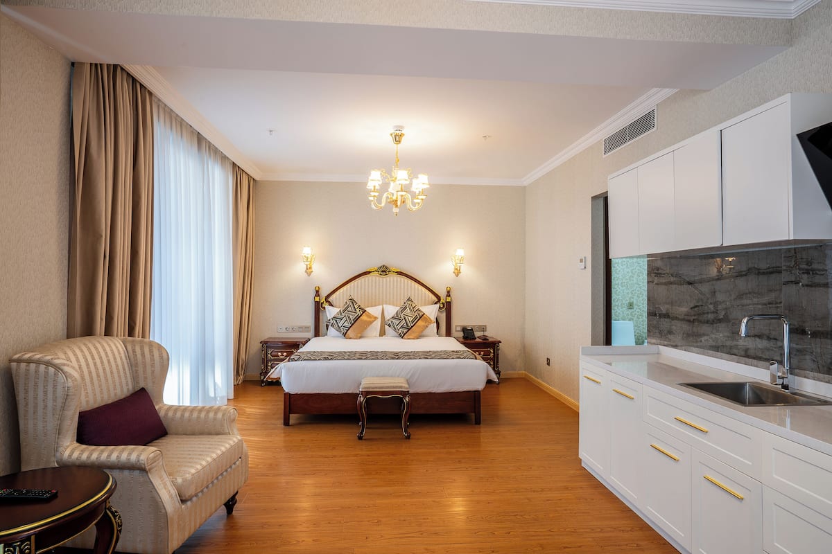 Ein Schlafzimmer mit einem großen Bett, Nachttischen, einem Sessel und einer Küchenzeile mit Spüle und Schränken.