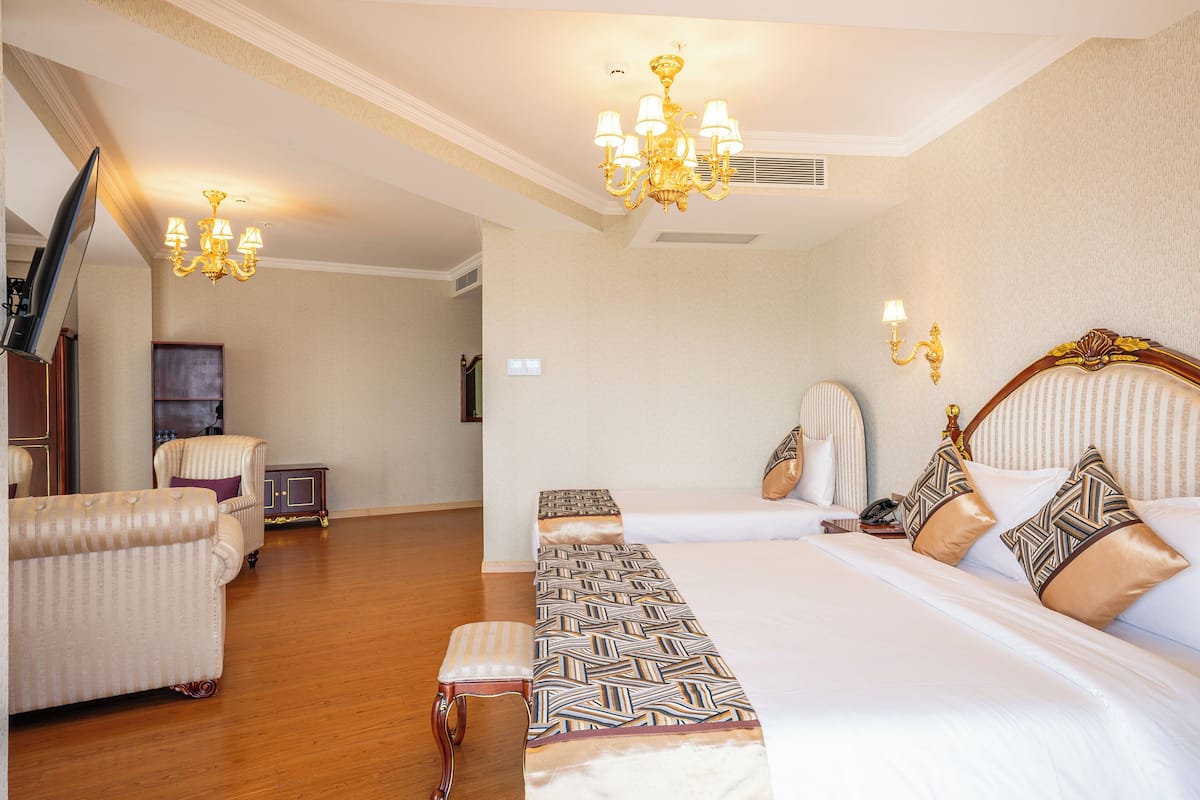 Ein Hotelzimmer mit einem großen Bett, einer Bank, einem Sessel, einem Fernseher und einer Kristallleuchtre.
