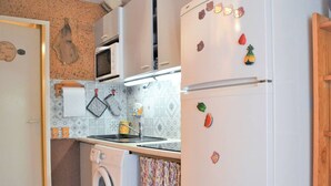 A compact kitchen with a washing machine, a microwave, and a refrigerator adorned with fruit magnets. - Charming 2-Bedroom Apartment with Pool and Terrace in Le Lavandou for 6 (Le Lavandou)