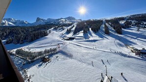 A snowy ski slope with a clear sky and mountains in the background.