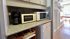 A kitchen with two white Brandt microwaves, a coffee maker, and a small refrigerator.