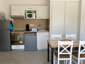 Eine kompakte Küche mit Mikrowelle, Backofen, Geschirrspüler und einer kleinen Spüle. Ein Esstisch mit Stühlen und ein Schrank mit einer Mikrowelle darüber.