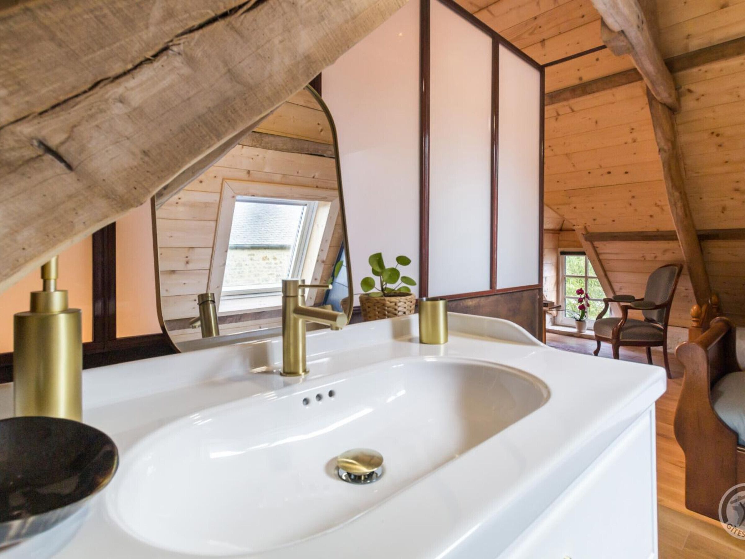 Une salle de bain avec un lavabo blanc, des robinets dorés et un plafond en bois.