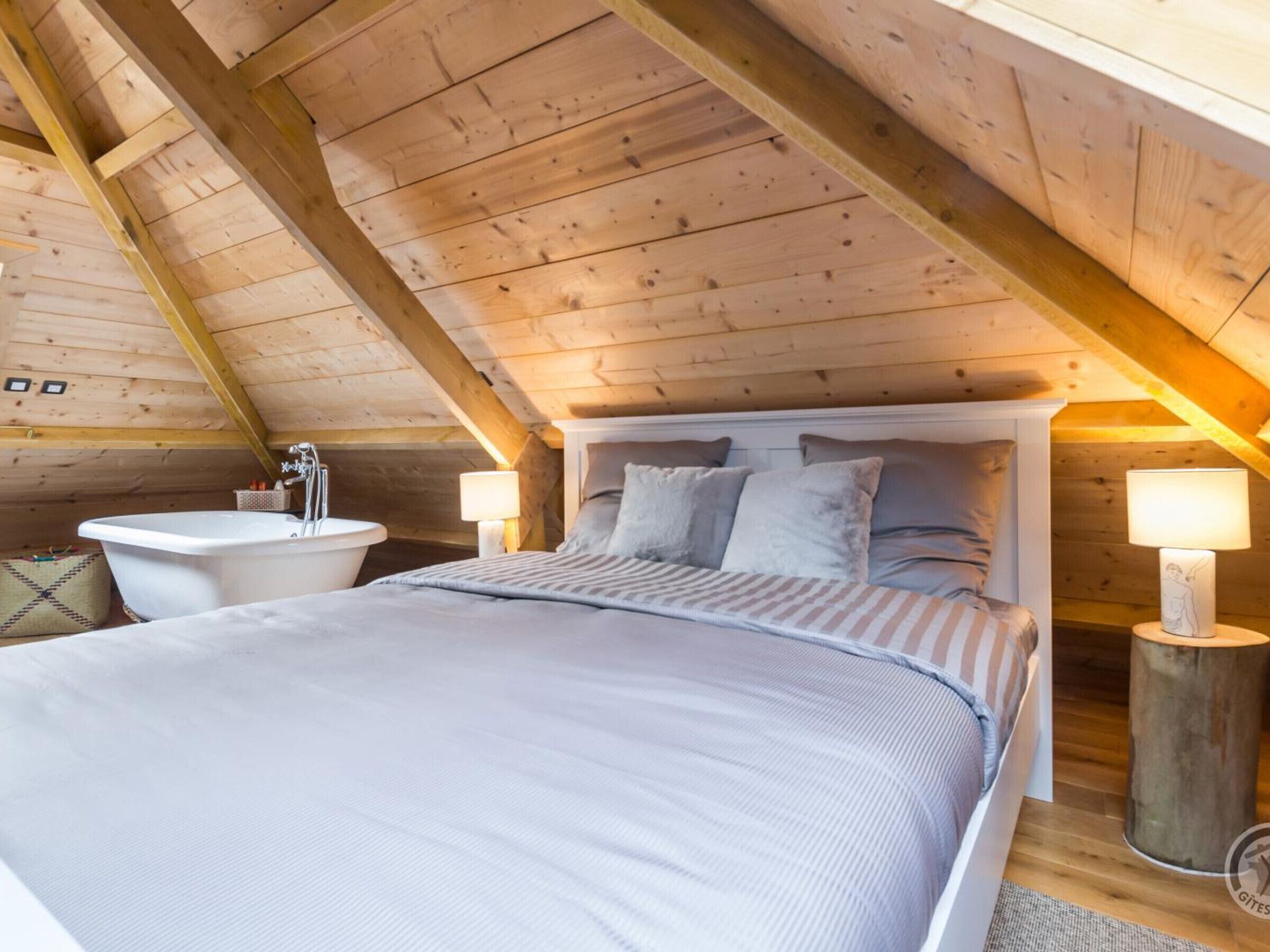 Un dormitorio acogedor en el ático, con una cama grande, una bañera blanca y dos lámparas de noche.