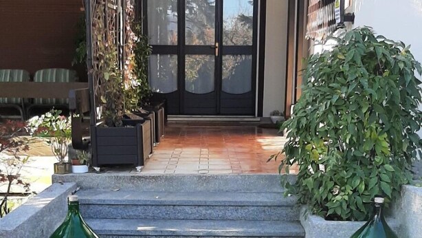 A brick pathway leading to a building entrance with a glass door, steps, and potted plants. - VILLA PARADIS B&B (Airuno)