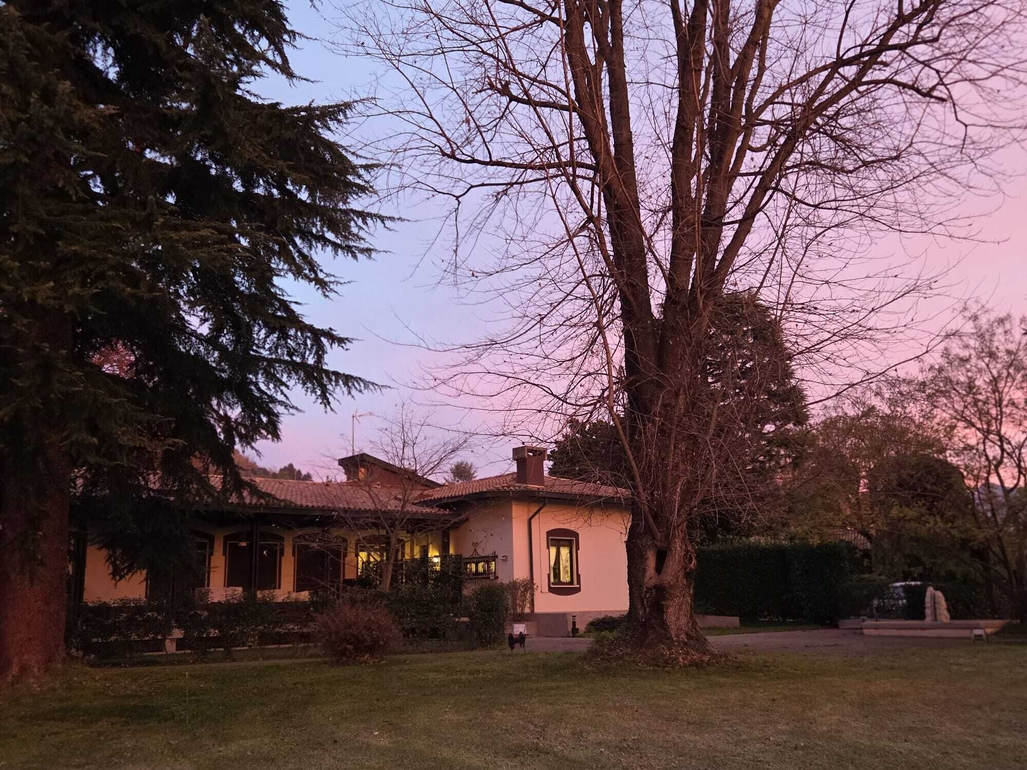 Uma casa de dois andares com telhado ladrilhado, rodeada por um gramado bem cuidado e árvores já crescidas.