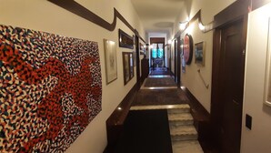 A hallway with framed artwork on the walls, a staircase, and a door with a newspaper on it. - VILLA PARADIS B&B (Airuno)