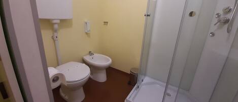 Un baño con inodoro, bidé y cabina de ducha con paredes de vidrio.