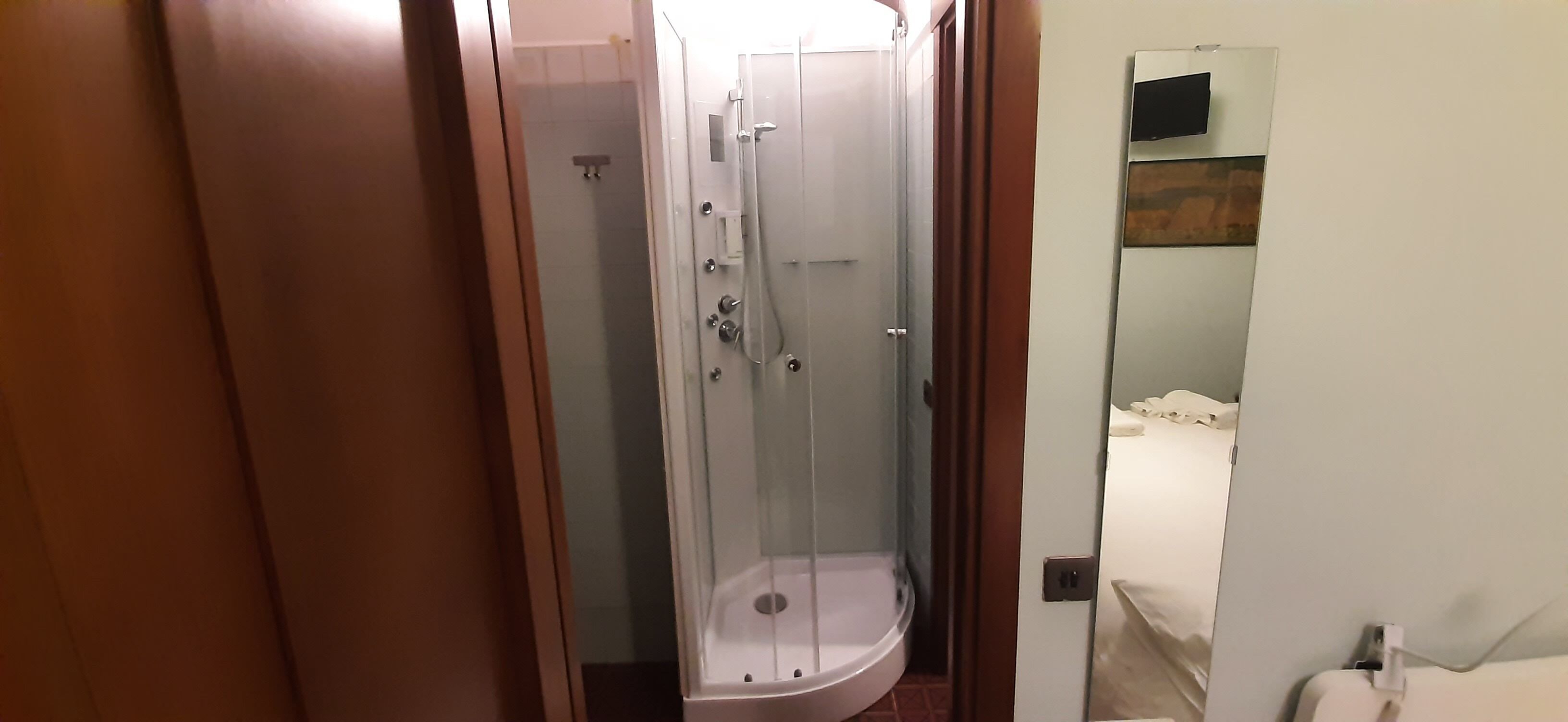 Un baño de hotel con ducha de vidrio, una cama con ropa blanca y una puerta de madera.